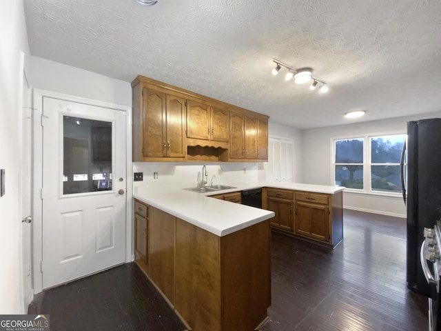 kitchen with brown cabinets, black appliances, a sink, dark wood finished floors, and a peninsula