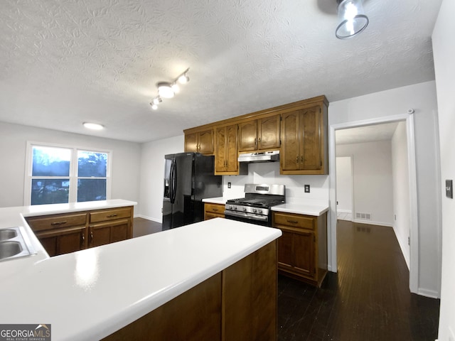 kitchen with under cabinet range hood, stainless steel range with gas cooktop, black fridge with ice dispenser, and light countertops