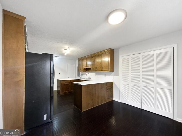 kitchen with a peninsula, dark wood-style floors, freestanding refrigerator, and light countertops