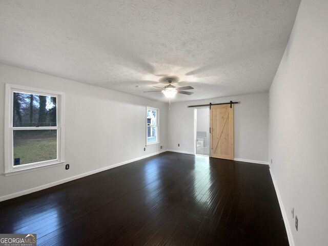 empty room featuring a barn door, baseboards, and dark wood-style flooring