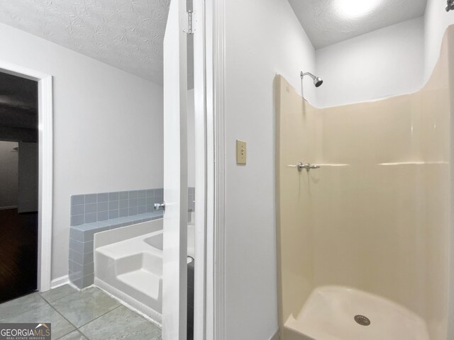 bathroom featuring tile patterned flooring, a shower stall, a bath, and a textured ceiling