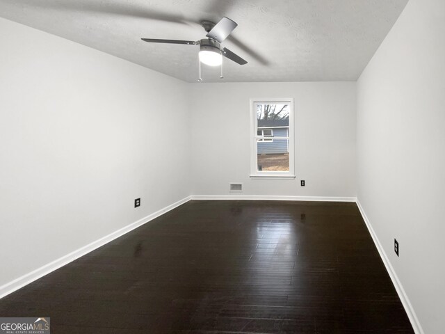 spare room featuring a ceiling fan, dark wood-style floors, visible vents, baseboards, and a textured ceiling