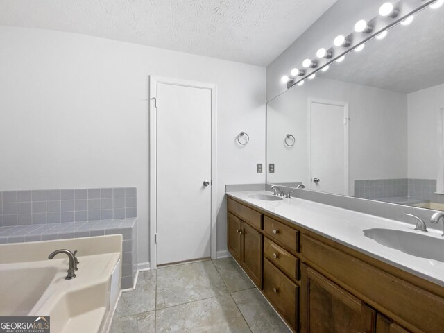 full bath featuring a sink, a textured ceiling, a bath, and double vanity