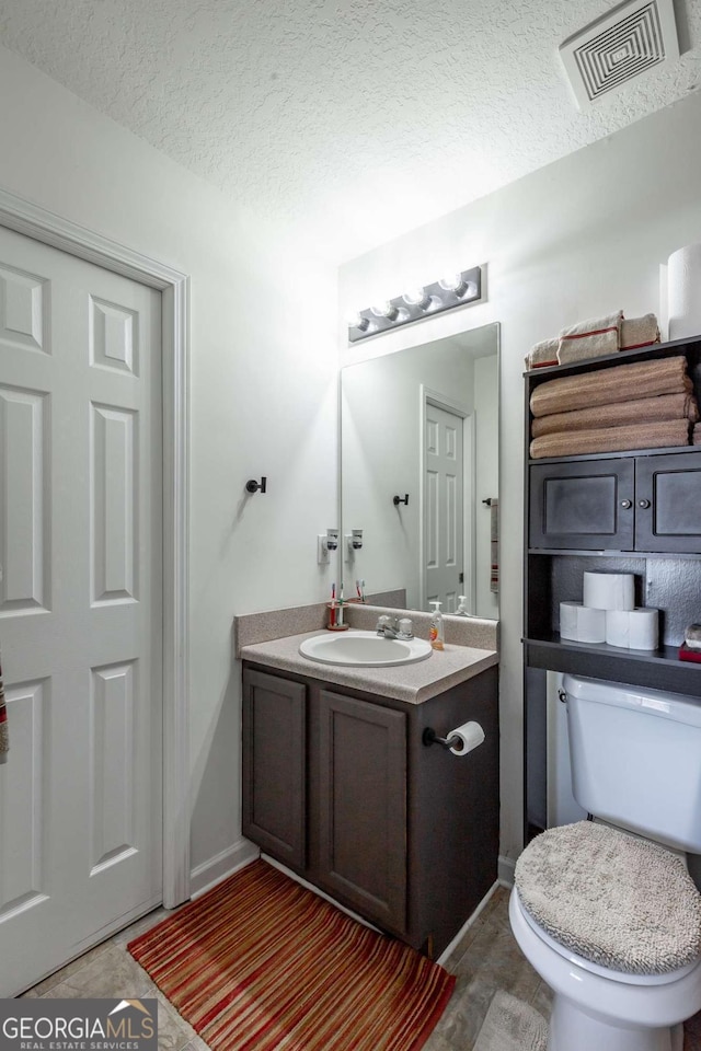 half bath featuring vanity, toilet, visible vents, and a textured ceiling