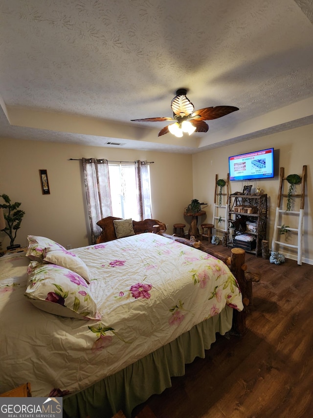 bedroom with a raised ceiling, a textured ceiling, wood finished floors, and a ceiling fan