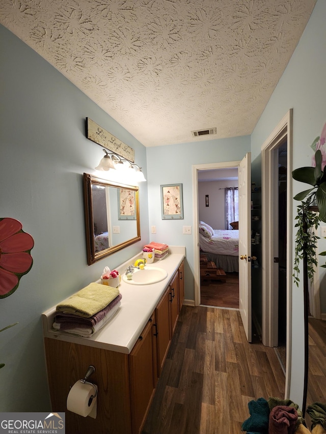 ensuite bathroom with visible vents, vanity, wood finished floors, ensuite bath, and a textured ceiling