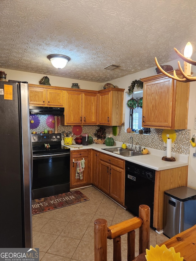 kitchen featuring backsplash, under cabinet range hood, light tile patterned floors, black appliances, and a sink