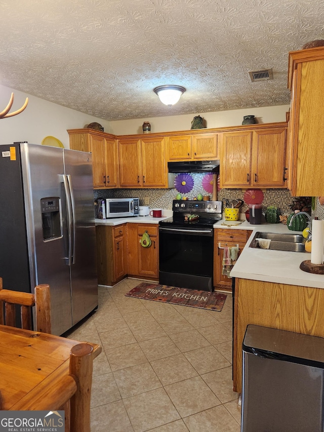 kitchen featuring visible vents, under cabinet range hood, brown cabinetry, stainless steel appliances, and a sink