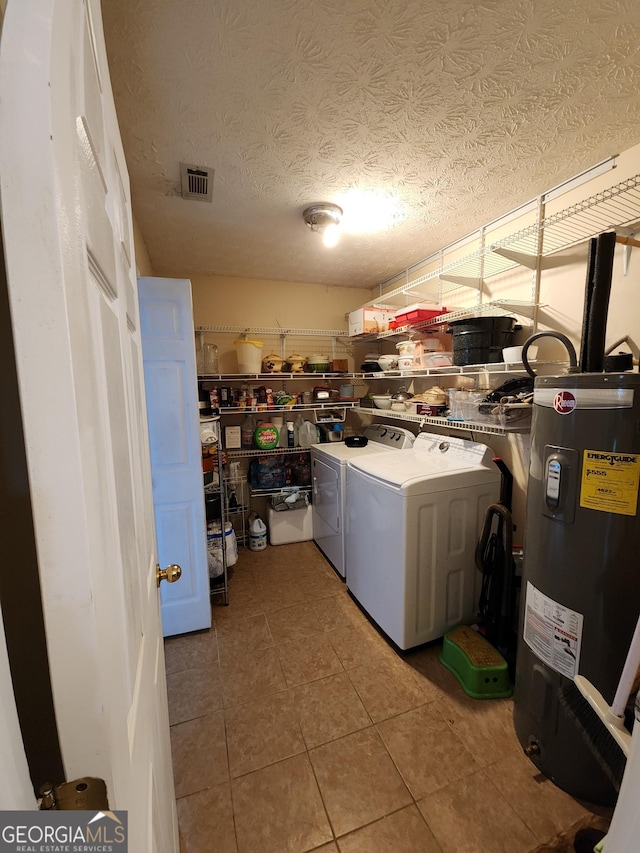 clothes washing area featuring visible vents, electric water heater, washing machine and dryer, light tile patterned floors, and laundry area