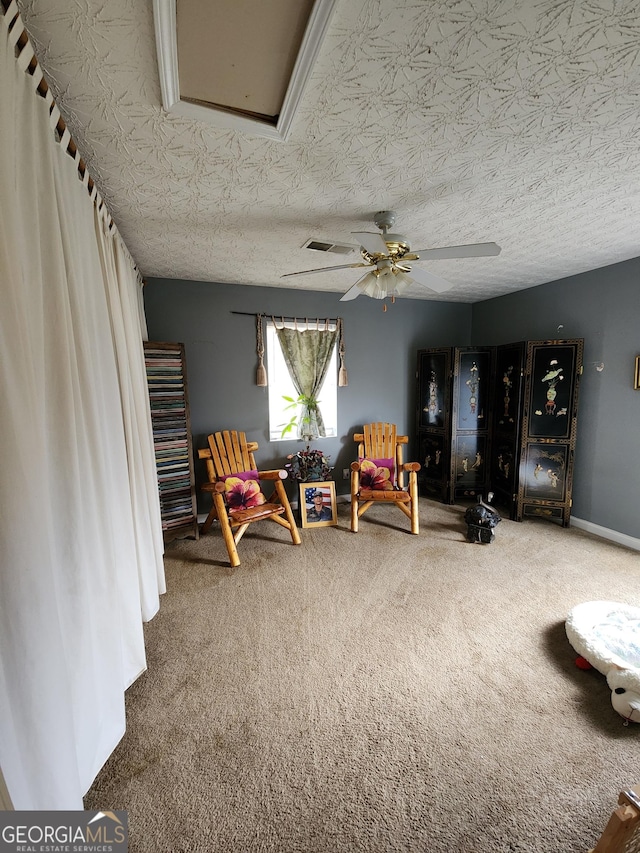 living area featuring visible vents, baseboards, carpet floors, a textured ceiling, and a ceiling fan