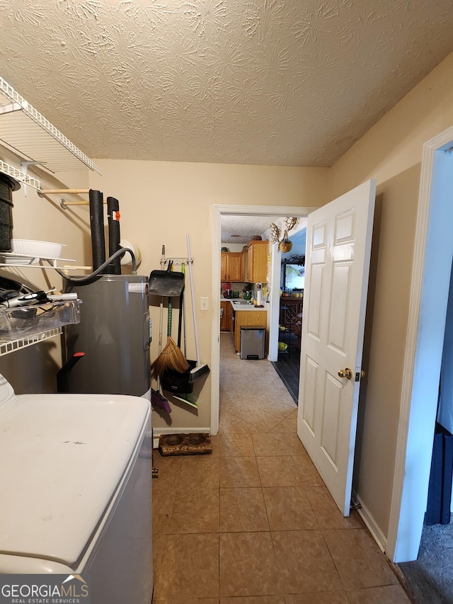 interior space featuring washer / clothes dryer, a textured ceiling, water heater, tile patterned flooring, and laundry area