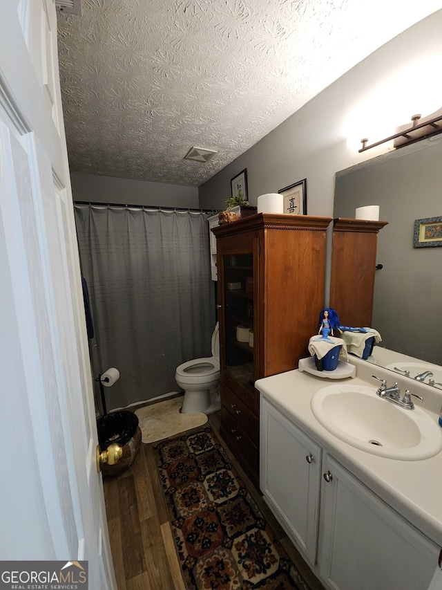 full bathroom with curtained shower, toilet, vanity, wood finished floors, and a textured ceiling