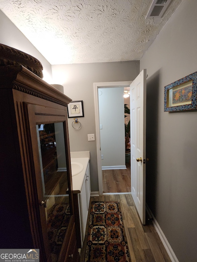 bathroom featuring visible vents, a textured ceiling, wood finished floors, baseboards, and vanity