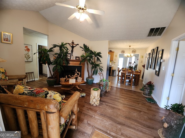 living area with visible vents, vaulted ceiling, ceiling fan with notable chandelier, wood finished floors, and a textured ceiling