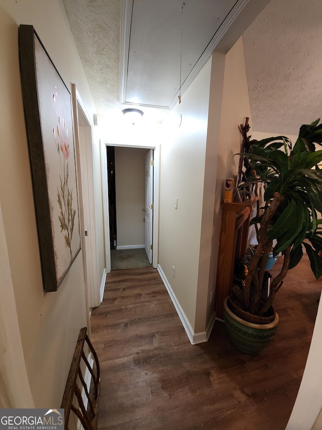 hall featuring attic access, wood finished floors, baseboards, and a textured ceiling