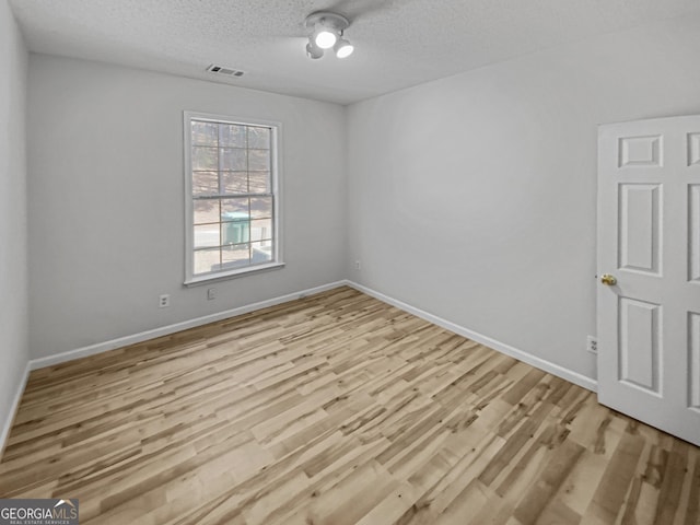 empty room featuring baseboards, wood finished floors, visible vents, and a textured ceiling