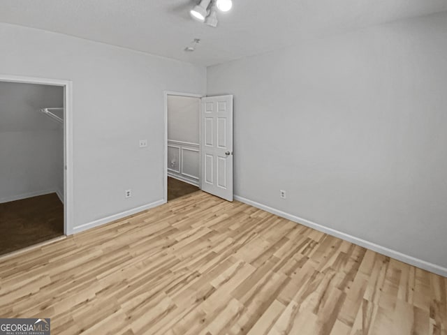 unfurnished bedroom with a walk in closet, baseboards, and wood finished floors