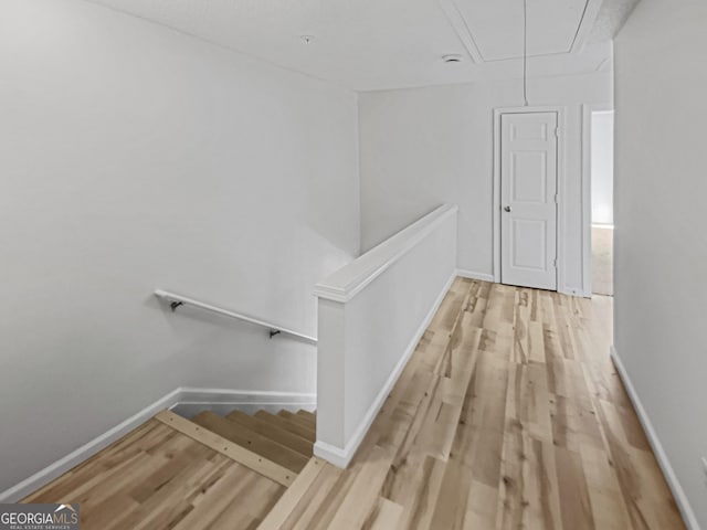 corridor featuring attic access, an upstairs landing, baseboards, and light wood finished floors