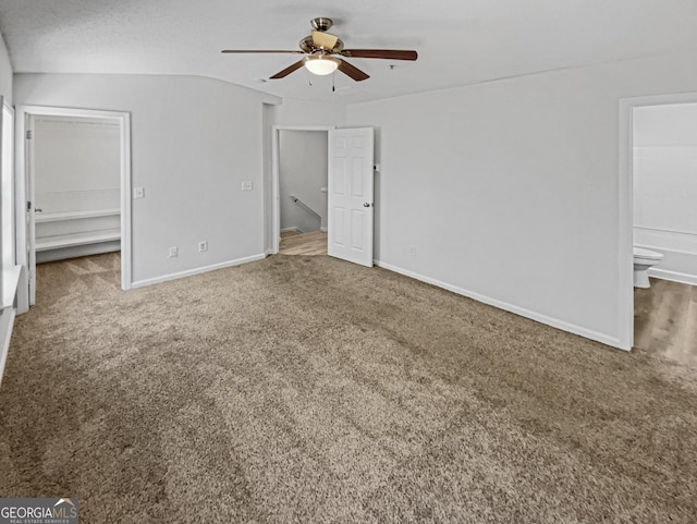 unfurnished bedroom featuring a walk in closet, ensuite bath, carpet flooring, and baseboards