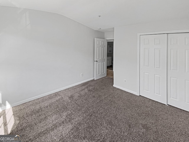 unfurnished bedroom featuring baseboards, lofted ceiling, a closet, and dark carpet