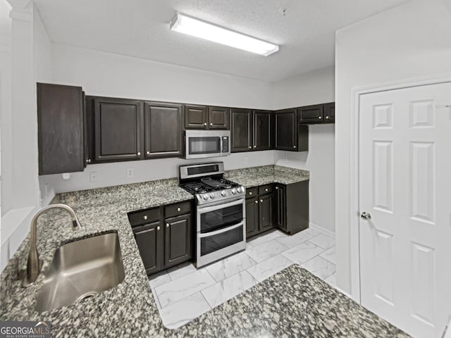 kitchen featuring marble finish floor, a sink, stone countertops, a textured ceiling, and appliances with stainless steel finishes