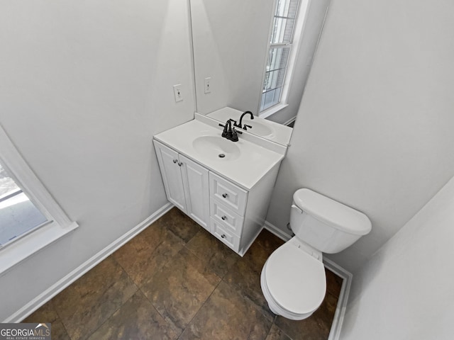 half bathroom featuring vanity, stone finish floor, toilet, and baseboards