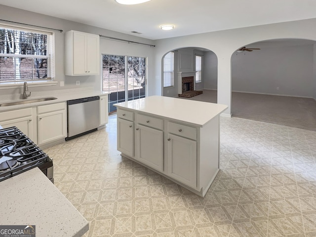 kitchen with dishwasher, a brick fireplace, light floors, and a sink