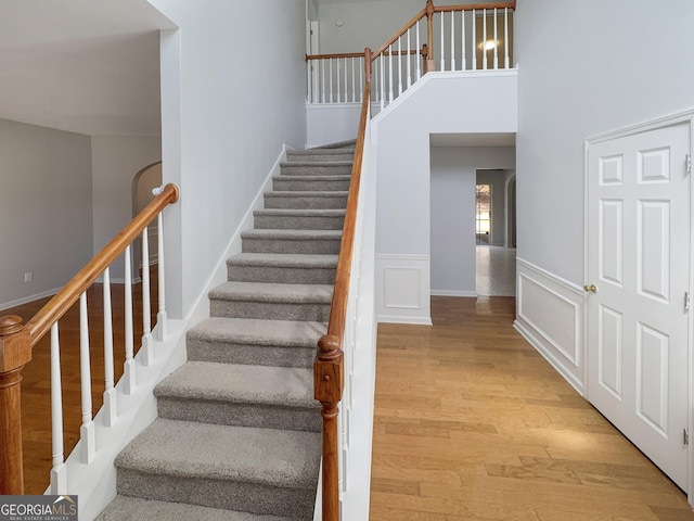 stairway with a high ceiling, a decorative wall, wood finished floors, and a wainscoted wall