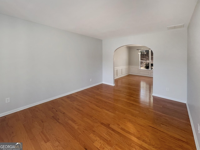 empty room with visible vents, wood finished floors, arched walkways, and baseboards