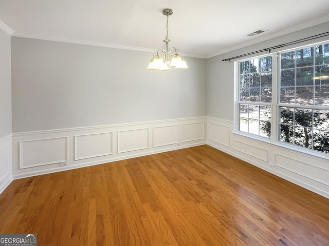 unfurnished dining area featuring a notable chandelier, crown molding, visible vents, and wood finished floors