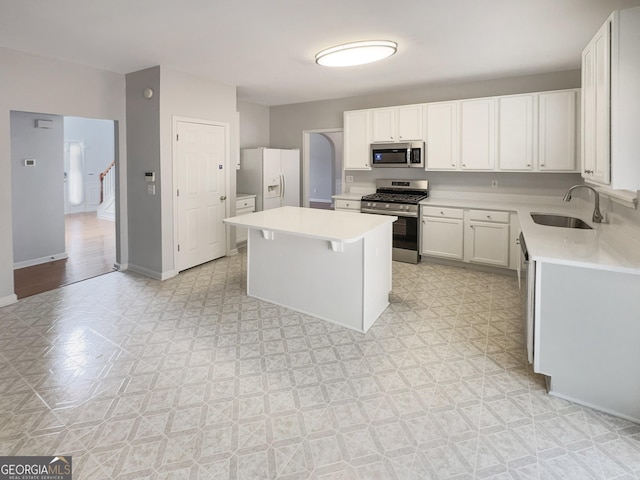 kitchen with baseboards, a kitchen island, a sink, light countertops, and appliances with stainless steel finishes