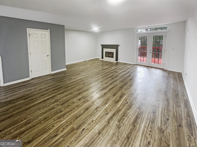 unfurnished living room with french doors, a fireplace with flush hearth, baseboards, and dark wood finished floors