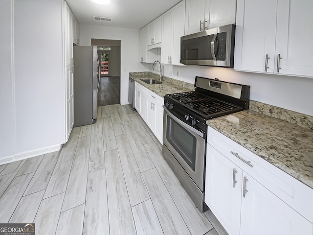 kitchen featuring white cabinets, appliances with stainless steel finishes, wood finish floors, and a sink