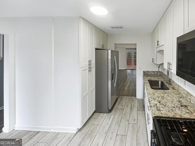 kitchen featuring visible vents, wood tiled floor, light stone counters, stainless steel appliances, and a sink