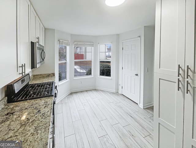 kitchen featuring stainless steel appliances, light stone countertops, wood tiled floor, and white cabinetry