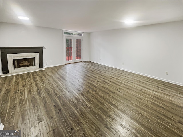 unfurnished living room with dark wood-type flooring, a fireplace with raised hearth, baseboards, and french doors