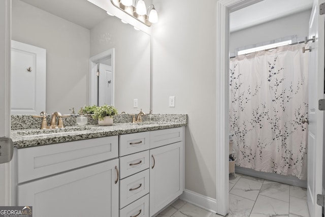 full bath with double vanity, baseboards, marble finish floor, and a sink