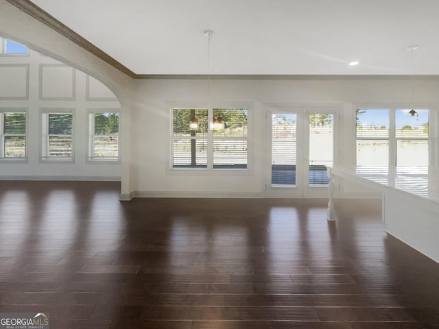 interior space with dark wood finished floors, crown molding, arched walkways, and baseboards