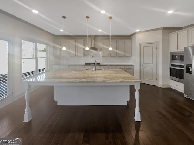 kitchen with a sink, backsplash, appliances with stainless steel finishes, wall chimney range hood, and dark wood-style flooring