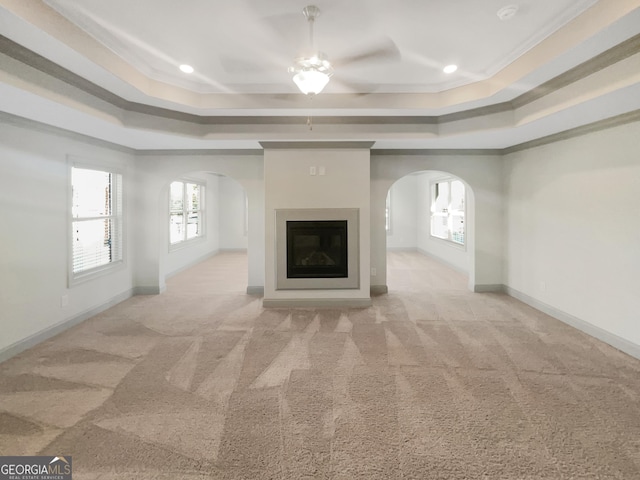 unfurnished living room featuring a wealth of natural light, arched walkways, and a tray ceiling