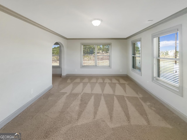 empty room featuring baseboards, arched walkways, light carpet, and ornamental molding