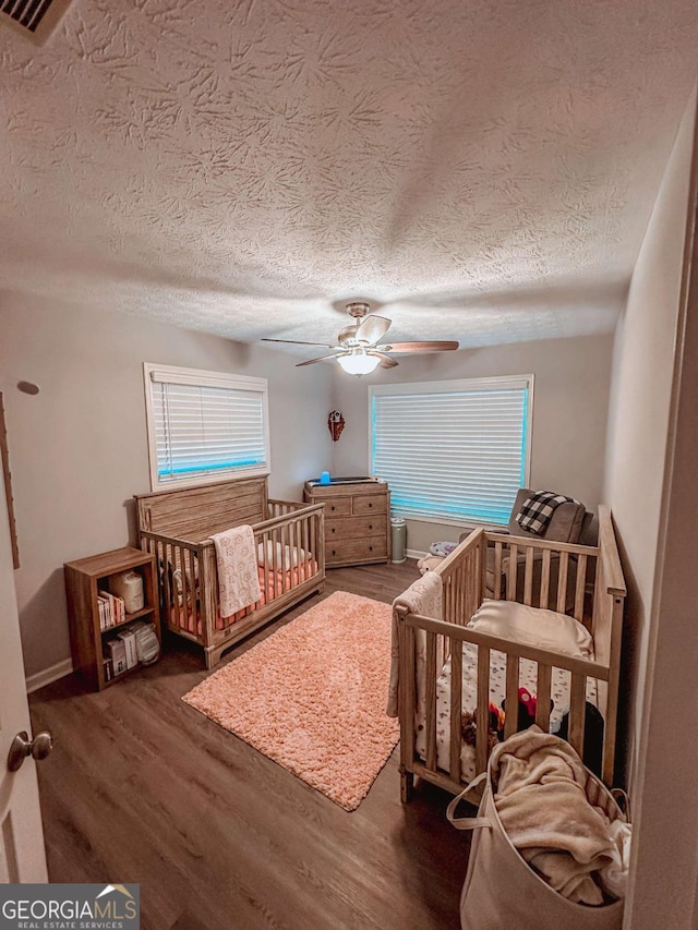 bedroom featuring a textured ceiling, wood finished floors, a crib, and ceiling fan