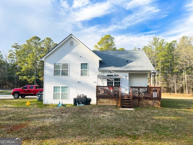 rear view of property featuring a yard, a deck, and a shingled roof