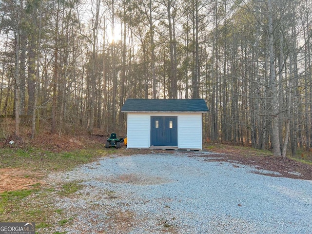 garage featuring gravel driveway, a storage unit, and a view of trees