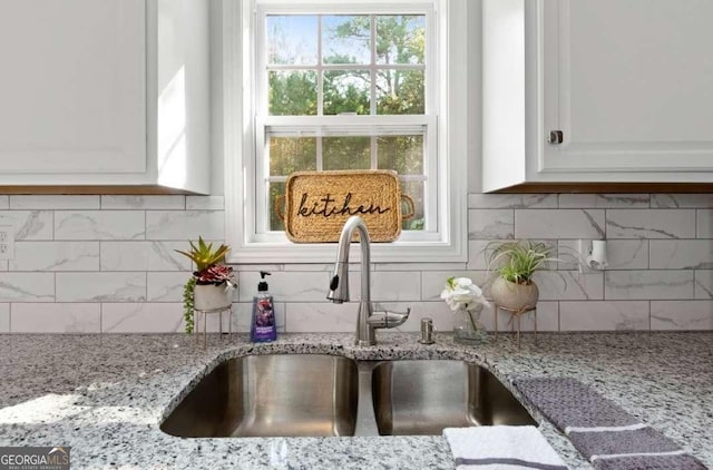 details featuring tasteful backsplash, white cabinets, light stone counters, and a sink