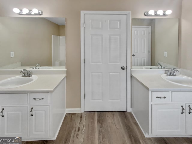 full bath featuring a sink, baseboards, two vanities, and wood finished floors