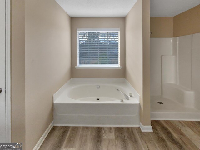 bathroom featuring a garden tub, wood finished floors, baseboards, and a shower