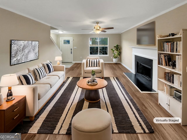 living room featuring a fireplace with raised hearth, crown molding, baseboards, ceiling fan, and wood finished floors