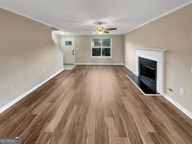 unfurnished living room featuring wood finished floors, a fireplace with raised hearth, and ornamental molding