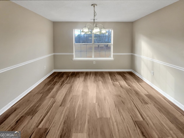 unfurnished dining area featuring wood finished floors, baseboards, and a chandelier